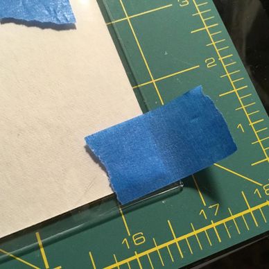 Blue painter's tape securing paper and glass on a cutting mat.