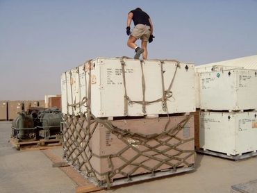 Person climbing on large secured cargo crates in an outdoor storage area.