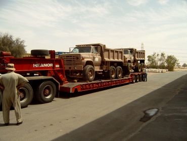 Two dump trucks loaded on a red trailer with two men nearby.