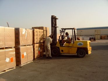 Worker operating forklift to move stacked boxes in warehouse yard.