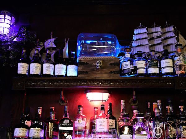 Dimly lit bar shelf with rum bottles and ship models.