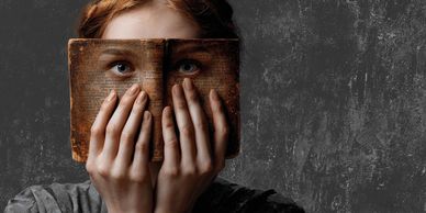 Person holds an old book covering their face with eyes visible through book cutouts.