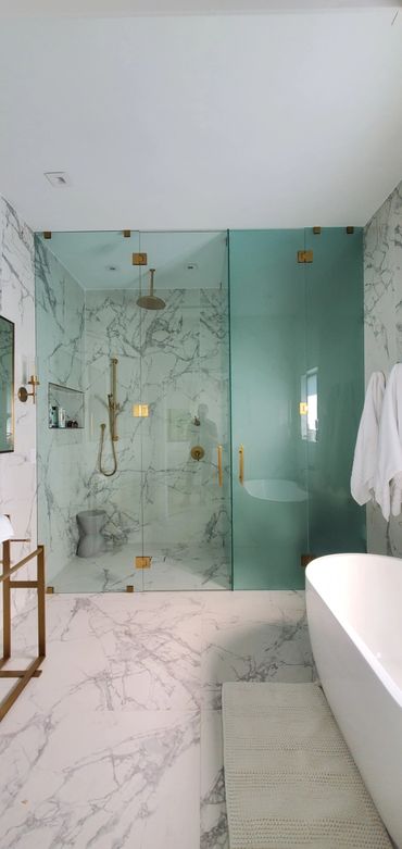 Modern bathroom with marble walls, glass shower doors, and gold fixtures.