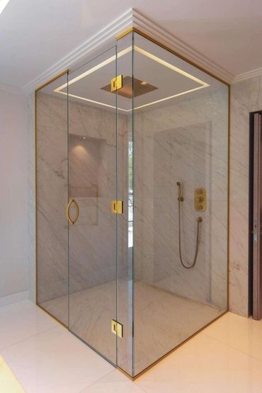 Modern glass shower enclosure with gold accents and marble walls.