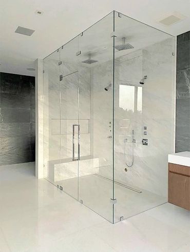 Modern bathroom with a spacious glass shower enclosure and marble walls.