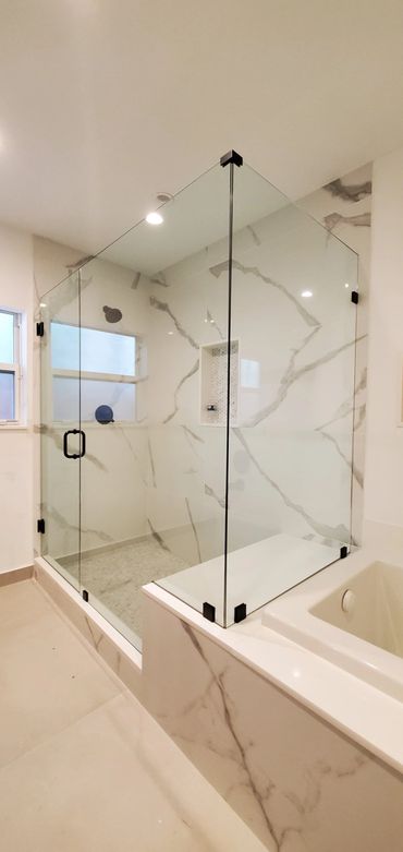 Modern bathroom with glass shower enclosure and marble walls.