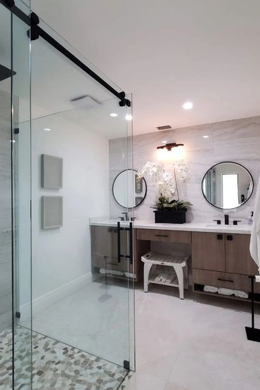 Modern bathroom with glass shower, round mirrors, wooden vanity, and white orchids.