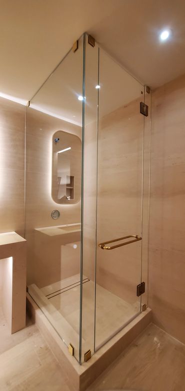 Minimalist beige bathroom with glass shower enclosure and gold fixtures.