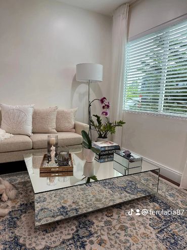 Modern living room with beige sofa, orchid, and reflective glass coffee table.