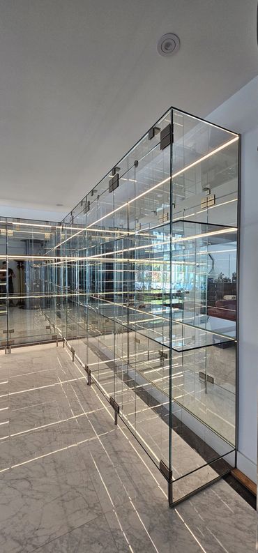 Modern glass display shelves with LED lighting reflecting on marble floor.