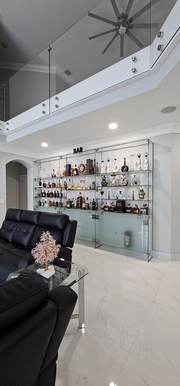 Modern home bar with glass shelves displaying various liquor bottles and decorative items.