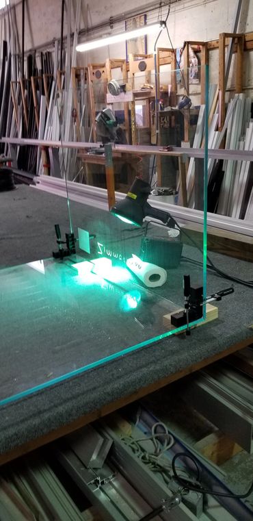 Glass panel being clamped and illuminated in a workshop.
