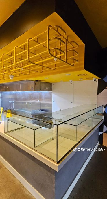 Modern commercial kitchen counter with glass partitions and yellow ceiling fixture.
