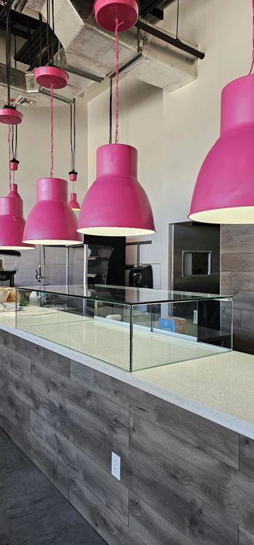 Modern cafe counter with bright pink hanging lamps and glass display case.