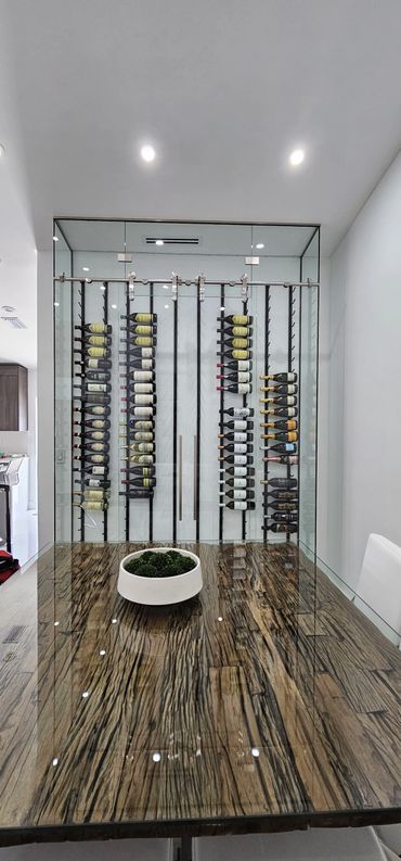 Modern wine cellar with glass doors behind a rustic wooden table.