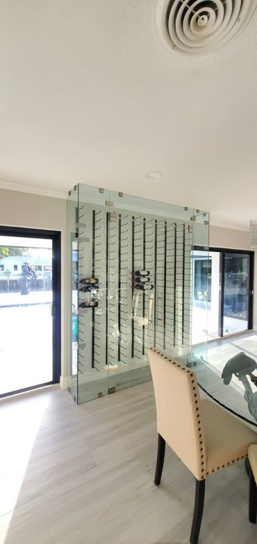 Modern glass wine rack in a bright dining area with beige chairs.