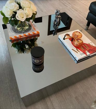 Modern reflective coffee table with books, flowers, and decorative items.