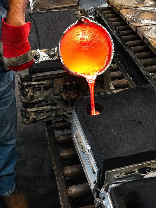 Worker pouring molten metal into a mold with protective gloves.