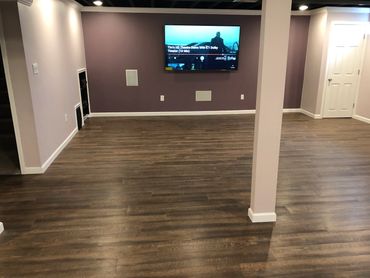 Basement entertainment area with built in wall mounted speakers and luxury vinyl plank flooring.