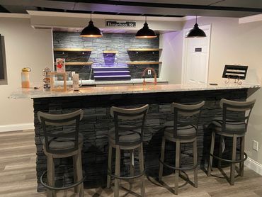 Custom basement wet bar, with bar height seating, stone backsplash, and luxury vinyl flooring.