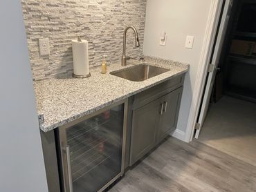 Wet bar with granite countertops, mini-fridge, and stone backsplash.