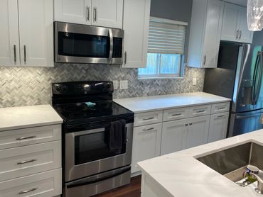 Remodeled kitchen with white shaker cabinets, marble backsplash, and quartz countertops.