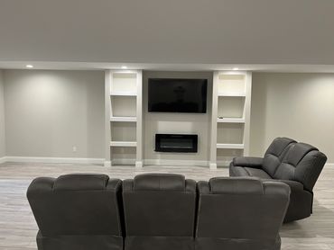 Basement entertainment area with custom shelving, wall mounted TV & wall mounted electric fireplace.