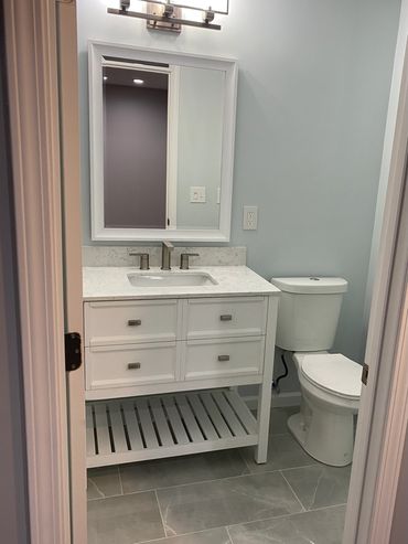 Porcelain tile with undercount sink vanity with open shelves and granite countertop and backsplash.