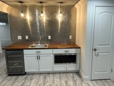 Basement wet bar with wine fridge, in-cabinet microwave, backsplash and butcher block countertops.