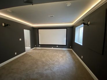Basement theatre room with projector, lighted crown moulding and in wall speaker system.