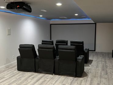Basement entertainment room/home theatre with recessed lighting, projector, wall mounted speakers.