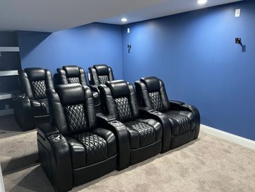 Basement entertainment room/home theatre with multi level seating, custom shelving, and wall mounts.