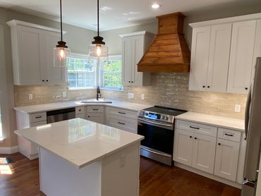 Newly remodeled kitchen with white shaker cabinets, custom range hood, and quartz countertops.