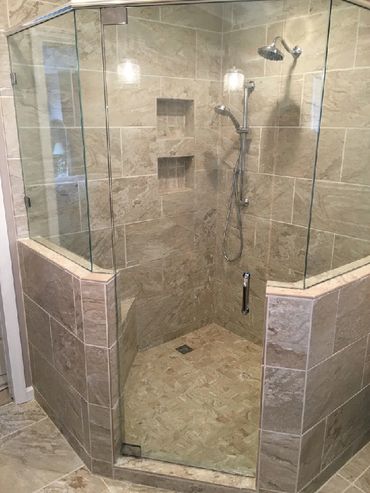 Travertine shower with glass surround, ledge, niches, rain shower head and handheld shower head.