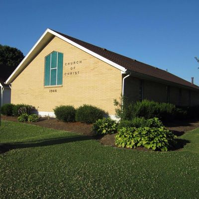 A brick church building with a stained glass window and neatly trimmed bushes.