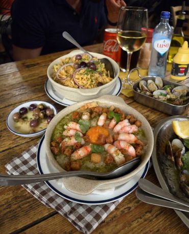 A table with seafood dishes, olives, and drinks including wine and soda.