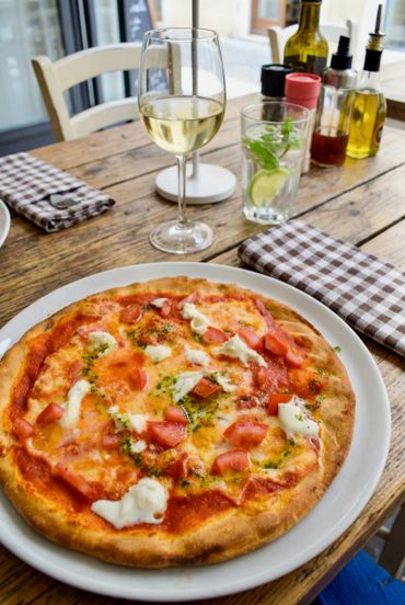 Fresh Margherita pizza with a glass of white wine on a wooden table.