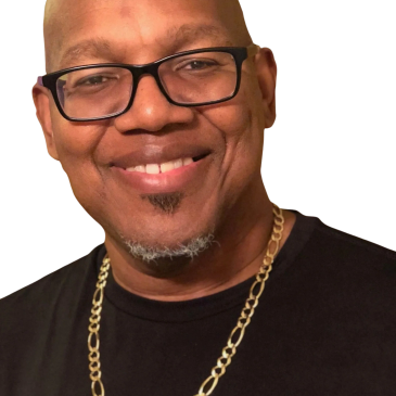 Smiling man wearing glasses, a gold chain, and a black shirt.