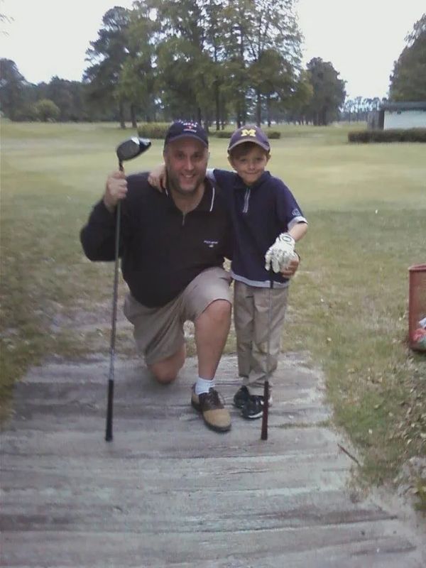 A man and a boy on a golf course posing with a golf club.