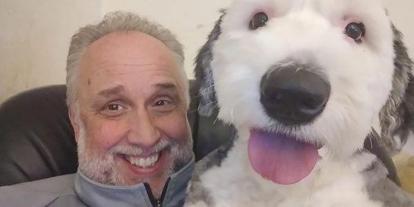 Man smiling with a large fluffy dog sticking out its tongue.