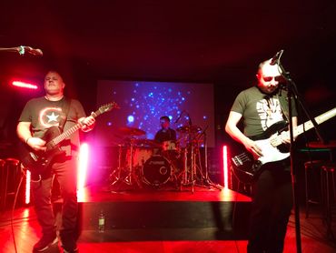 Band performing live with red and blue stage lights and a Captain America shirt.