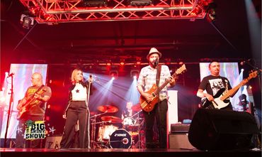 A live band performs energetically on stage with vibrant red lighting.