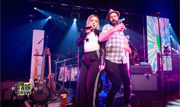 Two musicians performing energetically on stage with vibrant lighting.