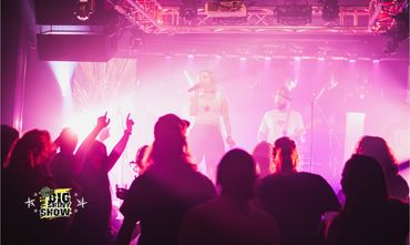 A vibrant live concert with a singer and guitarist illuminated by pink stage lights.