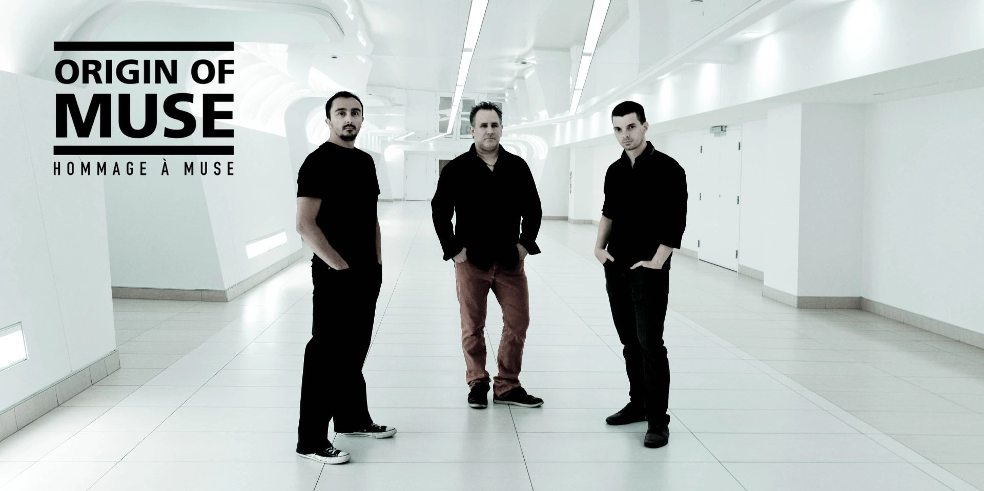 Three men standing in a modern white corridor with text "Origin of Muse".