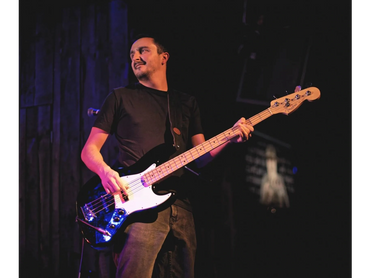 Man playing an electric bass guitar on stage in low light.