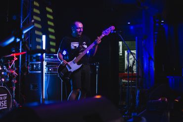 Musician playing bass guitar on stage under blue lighting.