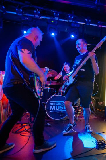 Band performs energetically on stage with blue and orange lighting.