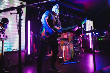 Guitarist passionately playing on a vibrant, neon-lit stage during a live performance.