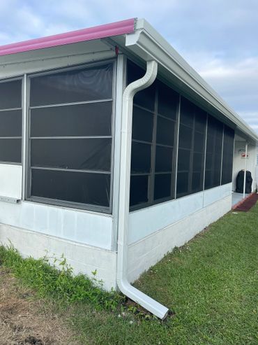 White gutter and downspout on a screened porch with a pink roof edge.